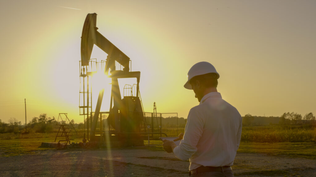 person holding a phone in front of an oil rig at sunrise